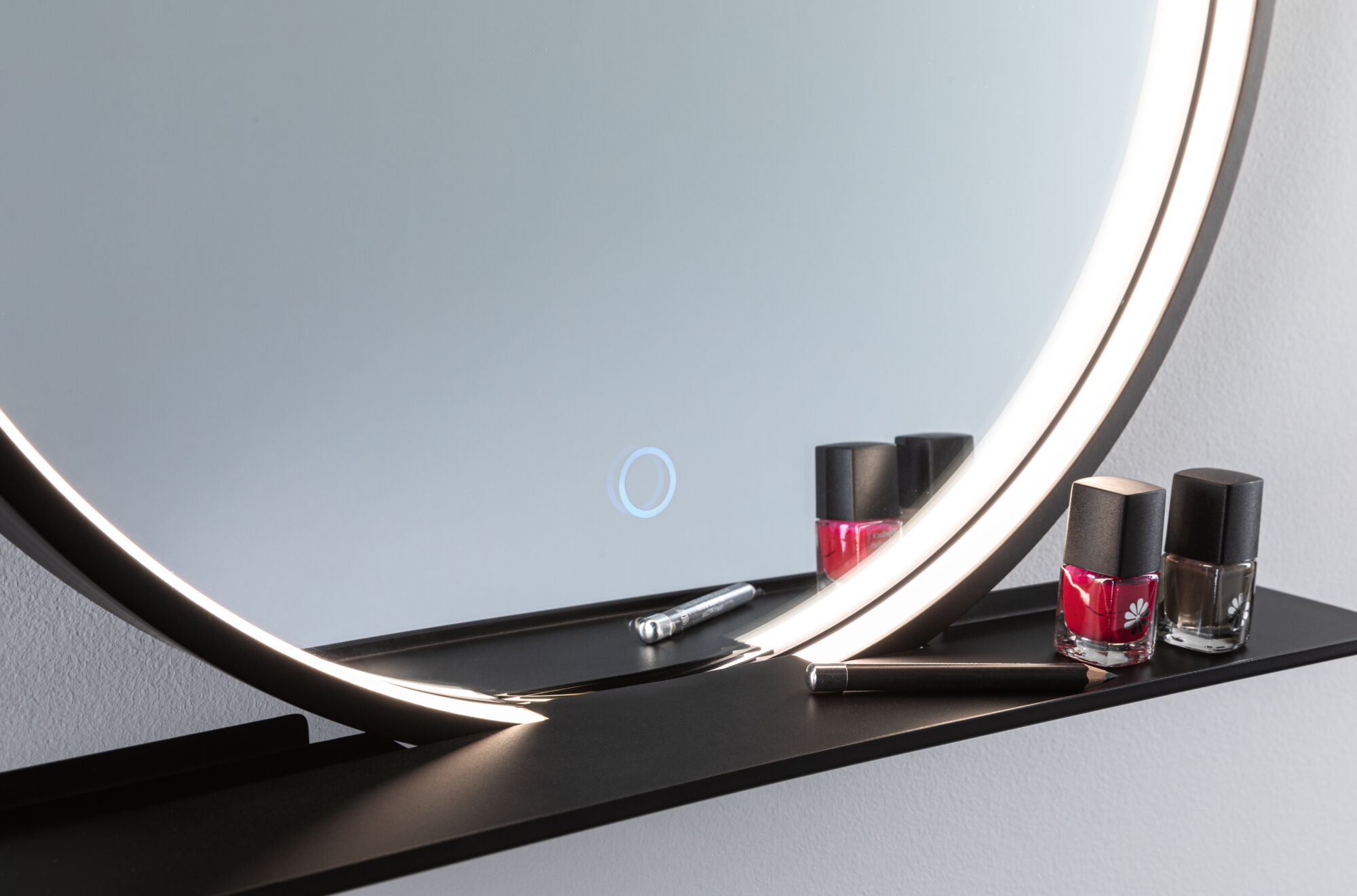 Ronde verlichte spiegel met zwart metalen plankje met rode en bruine nagellak en cosmetische potlood