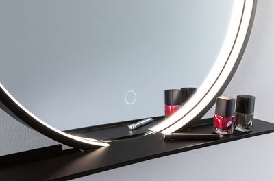 Ronde verlichte spiegel met zwart metalen plankje met rode en bruine nagellak en cosmetische potlood