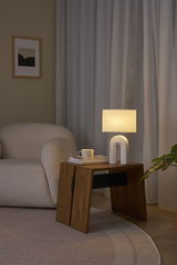 Modern white table lamp with fabric shade on wooden side table next to beige sofa in living room.