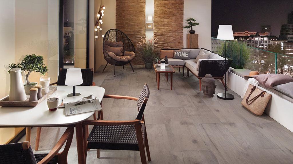 Balcon moderne avec sol en carreaux bois gris, coin salon confortable et lampe LED d'ambiance.