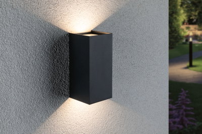 Zwarte aluminium wandlamp met warm wit licht naar boven en beneden op grijze buitenmuur