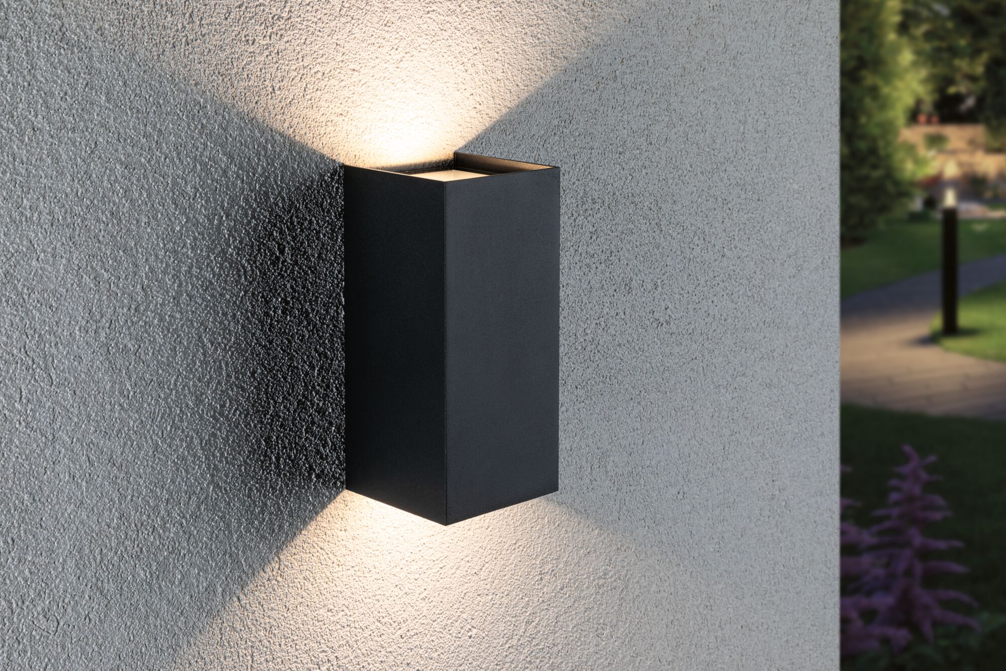 Black aluminium wall light with warm white up and down lighting on grey exterior wall
