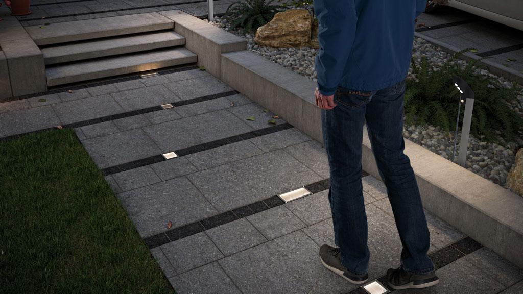 Oplyst havegang med indbyggede LED-gulvlys i grå stenfliser og sort stribemønster.