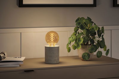 Moderne Tischlampe mit Zylindersockel aus Beton und warm leuchtender Glühbirne für stimmungsvolle Beleuchtung