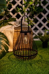 Black metal lantern with LED light on green grass, decorative outdoor garden lighting for ambiance