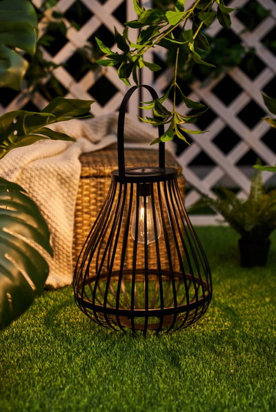 Black metal lantern with LED light on green grass, decorative outdoor garden lighting for ambiance
