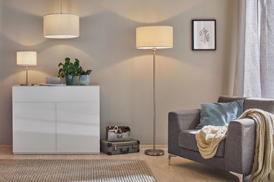 Moderne woonkamer met grijze stoffen fauteuil, wit dressoir en drie crèmekleurige lampen voor sfeerverlichting