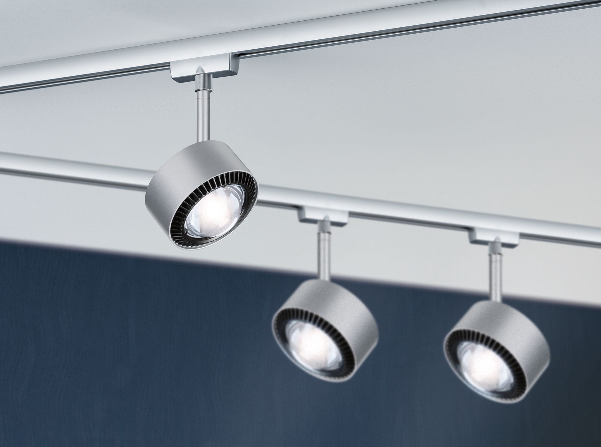 Drie zilverkleurige metalen LED-railspots gemonteerd aan wit plafond voor moderne verlichting