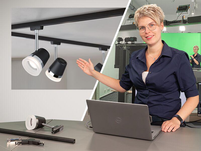 Frau präsentiert schwarze und weiße LED-Schienenstrahler aus Aluminium im Studio mit Laptop und grünem Hintergrund.