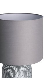 Tischlampe mit grauem Stoffschirm und gemustertem Keramikfuß in Weiß und Grau für Wohnräume.