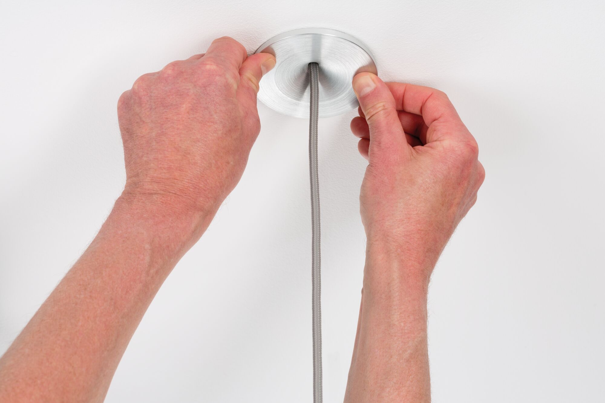 Hands installing round brushed aluminum ceiling mount with grey fabric cable for pendant light