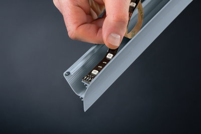 Hand plaatst zwarte LED-strip in grijs aluminium profiel voor strakke lichtinstallatie