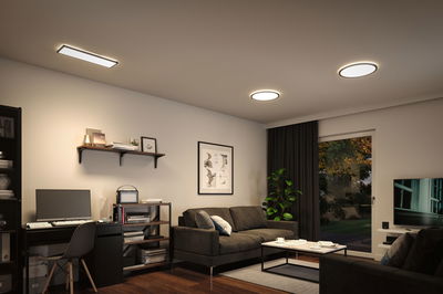 Modernes Wohnzimmer mit schwarzen Möbeln und drei weißen LED-Deckenleuchten für stimmungsvolle Raumbeleuchtung