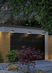 Modern black outdoor wall lights illuminate garage door with wooden cladding and garden plants at dusk