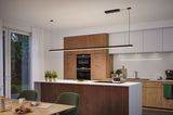 Moderne Küche mit Holzfronten und weißer Arbeitsplatte, LED-Pendelleuchte in Schwarz über Kochinsel.