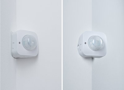 White plastic motion sensor mounted on indoor corner for automated lighting control