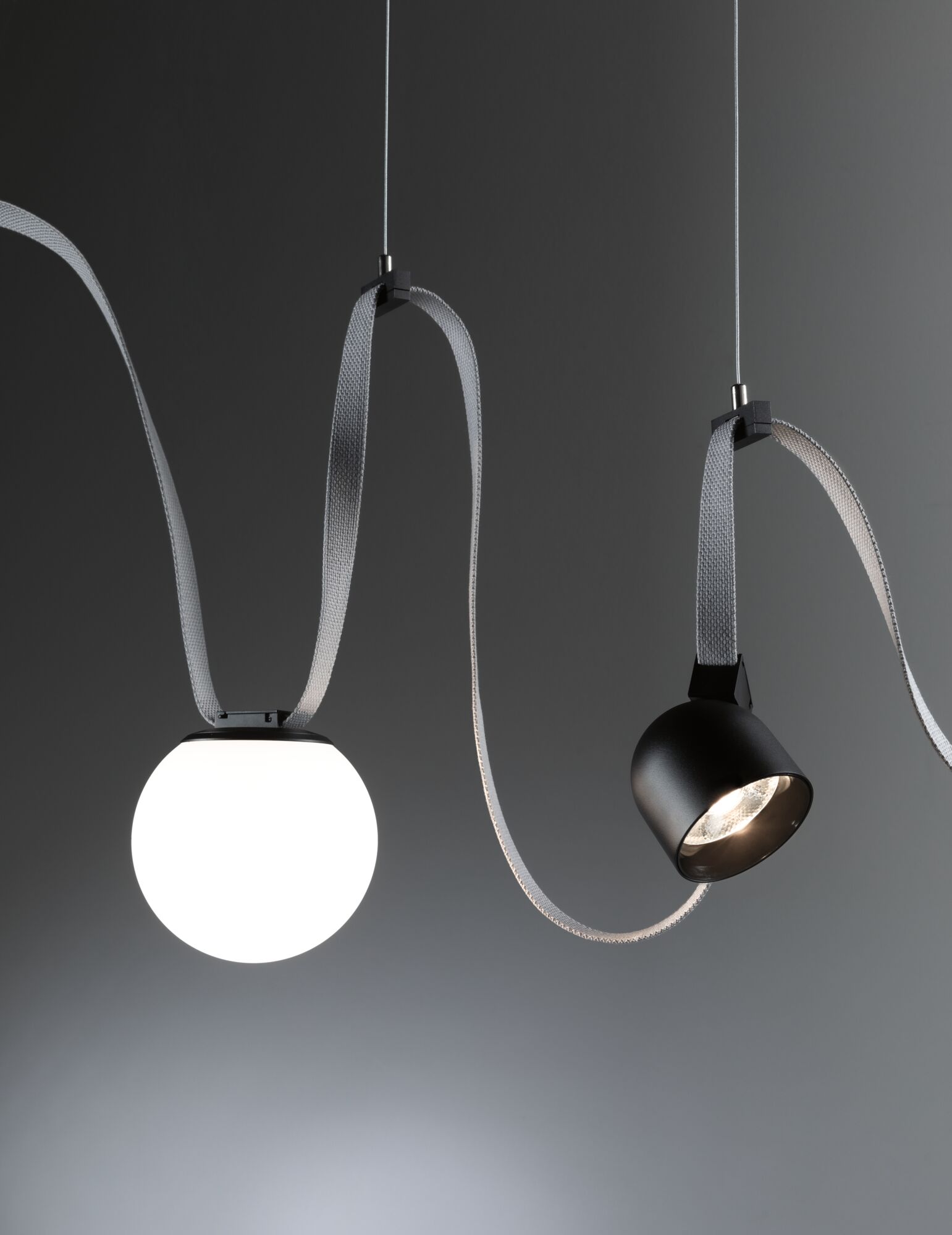 Moderne Pendelleuchte mit weißem Glasball und schwarzem Metallstrahler an grauem Textilkabel