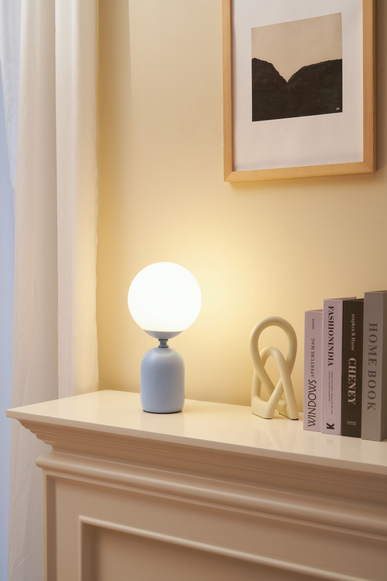 Modern table lamp with white glass and grey ceramic base on cream mantel with books and decor.