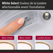 Main réglant la couleur de la lumière sur un plafonnier blanc avec anneau en bois