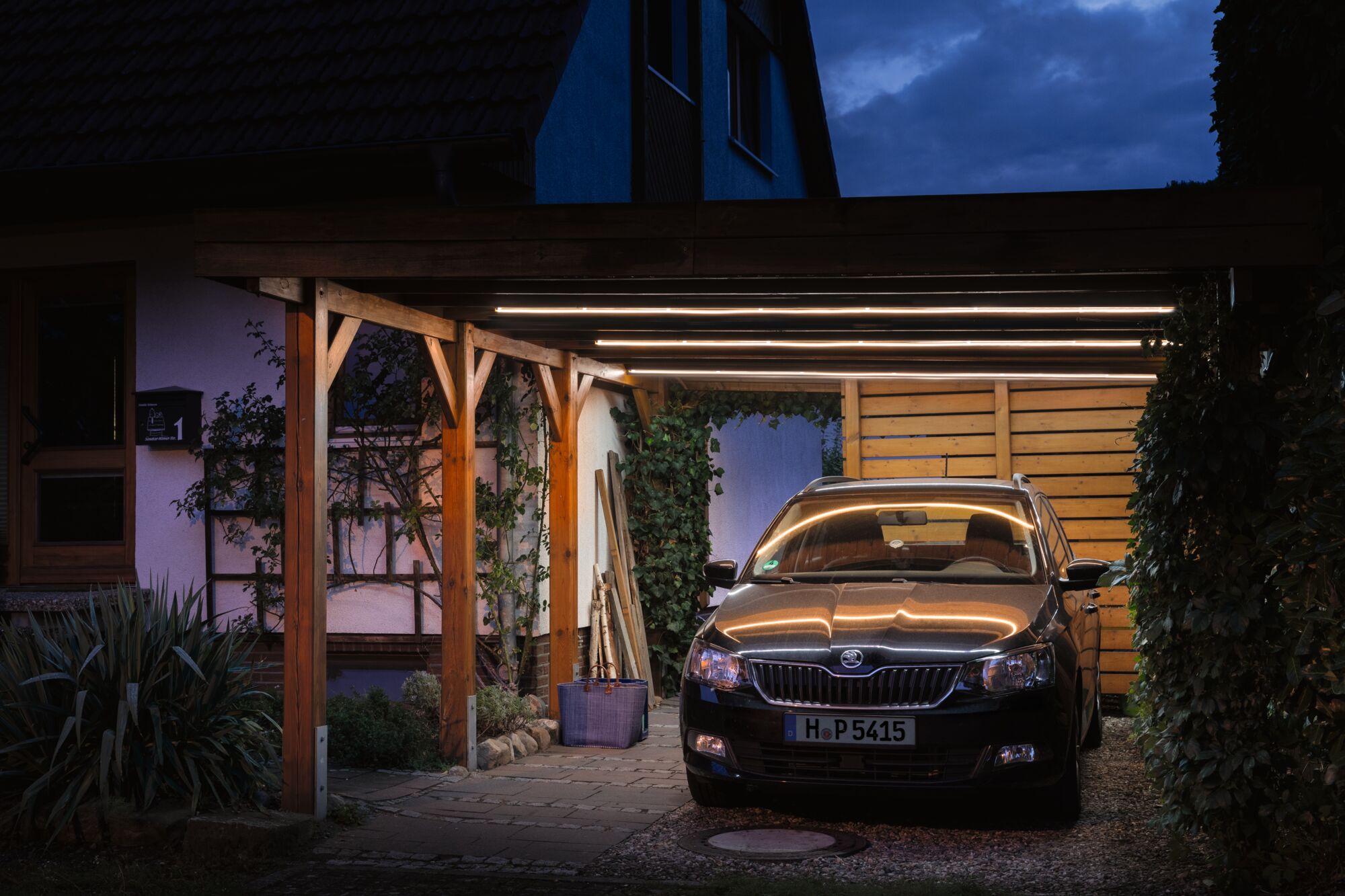 Houten carport met warmwitte LED-lichtstrips die zwarte auto bij schemering in tuin verlichten