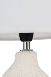Nærbillede af hvid keramisk lampe med sorte pletter og krommet metaldel til indendørs belysning