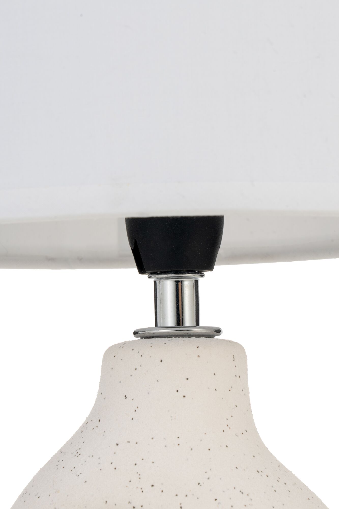Nærbillede af hvid keramisk lampe med sorte pletter og krommet metaldel til indendørs belysning