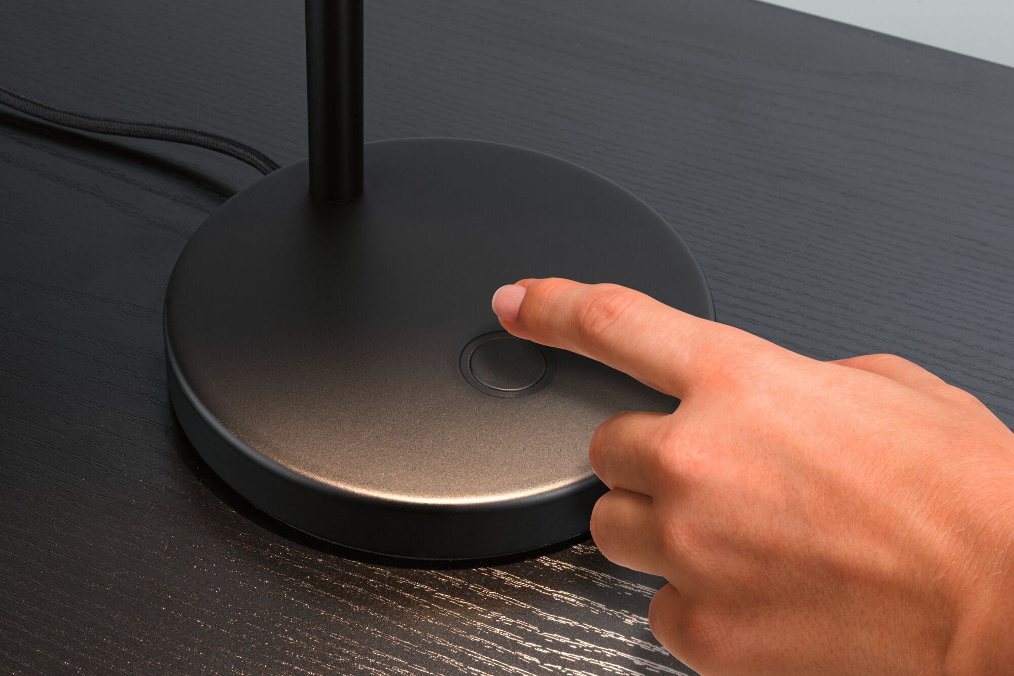 Hand drukt zwarte metalen bureaulamp schakelaar op donkere houten tafel voor LED-verlichting