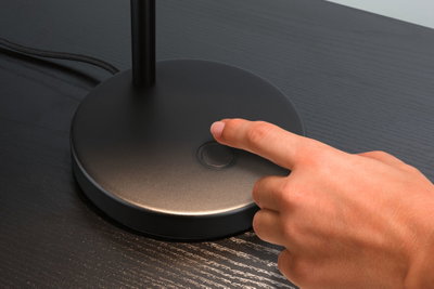 Hand drückt schwarzen Metall-Tischlampen-Schalter auf dunklem Holztisch für LED-Beleuchtung