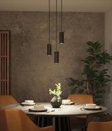 Three black metal pendant lights above round dining table with brown chairs and flower vase