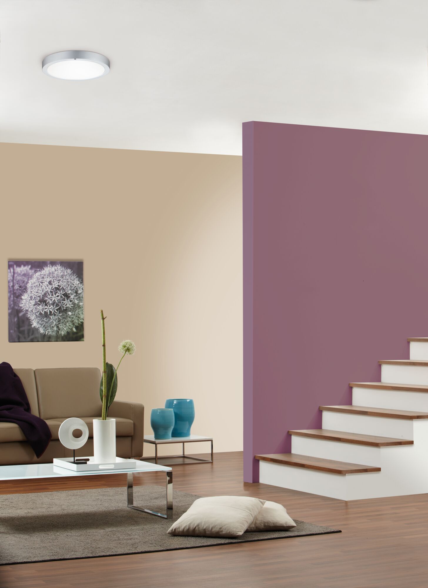 Runde Deckenleuchte mit weißem Diffusor und silbernem Rand in modernem Wohnzimmer mit Treppe.