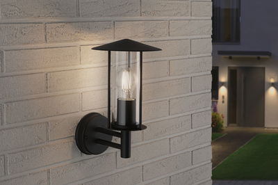 Black metal outdoor wall light with clear glass and visible LED bulb mounted on brick wall.