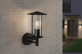 Schwarze Außenwandleuchte aus Metall mit klarem Glas und sichtbarer LED-Glühbirne an Hauswand.