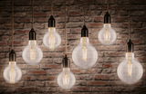 Seven hanging filament light bulbs with warm white glow against red brick wall, lighting design