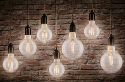 Sieben hängende Filament-Glühbirnen mit warmweißem Licht vor roter Backsteinwand, Beleuchtungskonzept