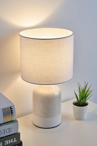 Moderne tafellamp met crèmekleurige keramische voet en lichte stoffen kap voor sfeervolle verlichting