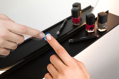 Hand bedient schwarzen Touch-Schalter an Kosmetikspiegel mit Nagellack und Kajalstift.