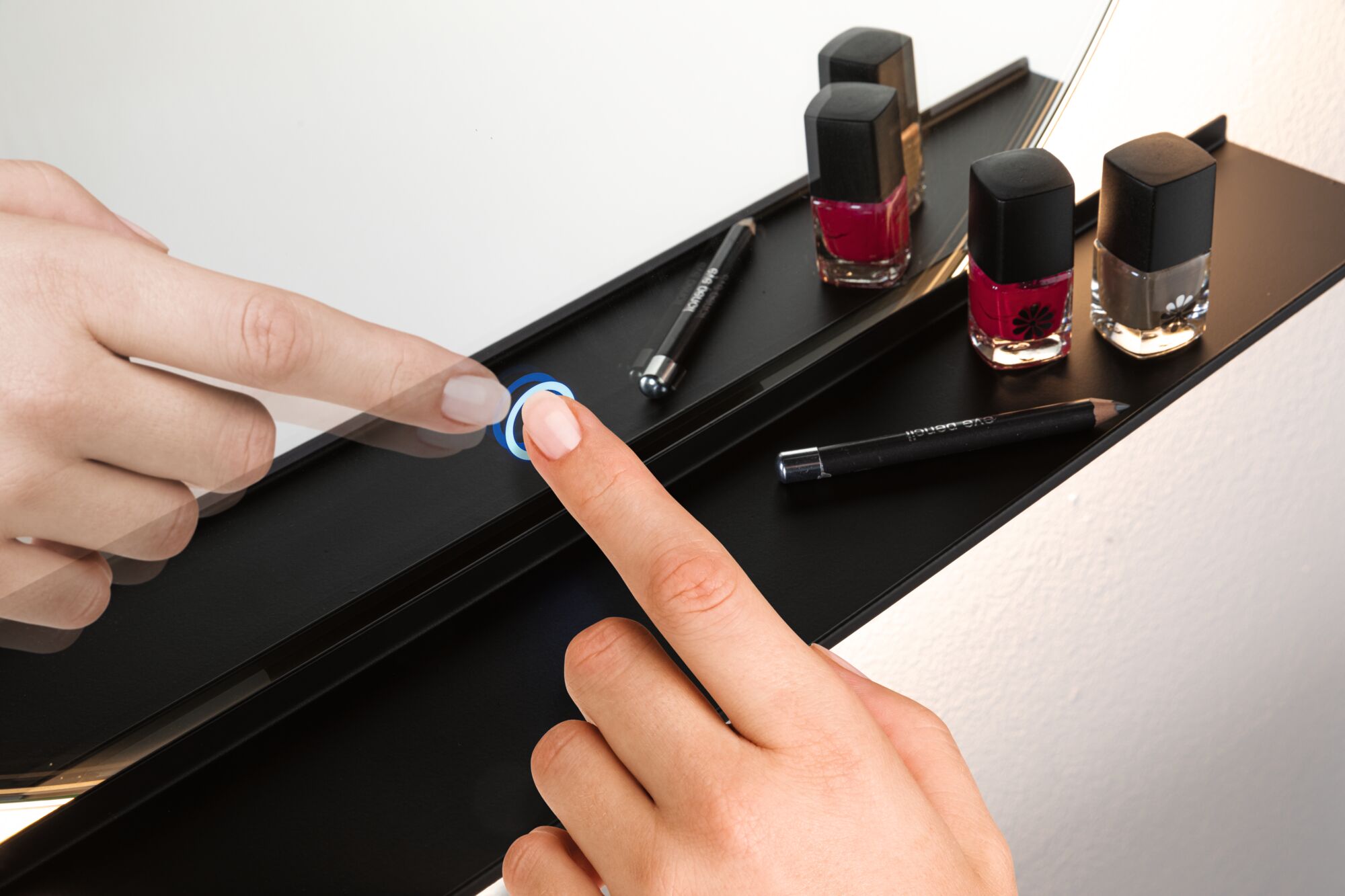 Hand operating black touch switch on vanity mirror with nail polish and eyeliner pencil.