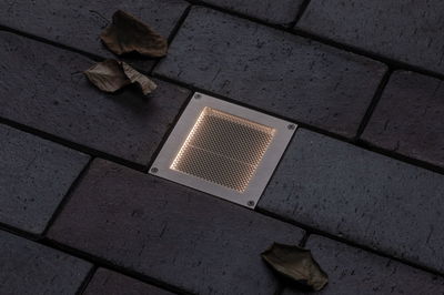Recessed square LED floor light in stainless steel with warm white glow on dark pavement surface.