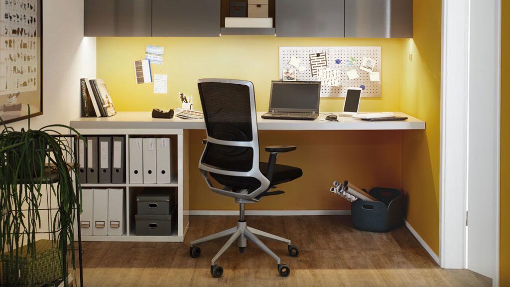 Modernes Home-Office mit ergonomischem Bürostuhl, Laptop und gelber Wandbeleuchtung für produktives Arbeiten.