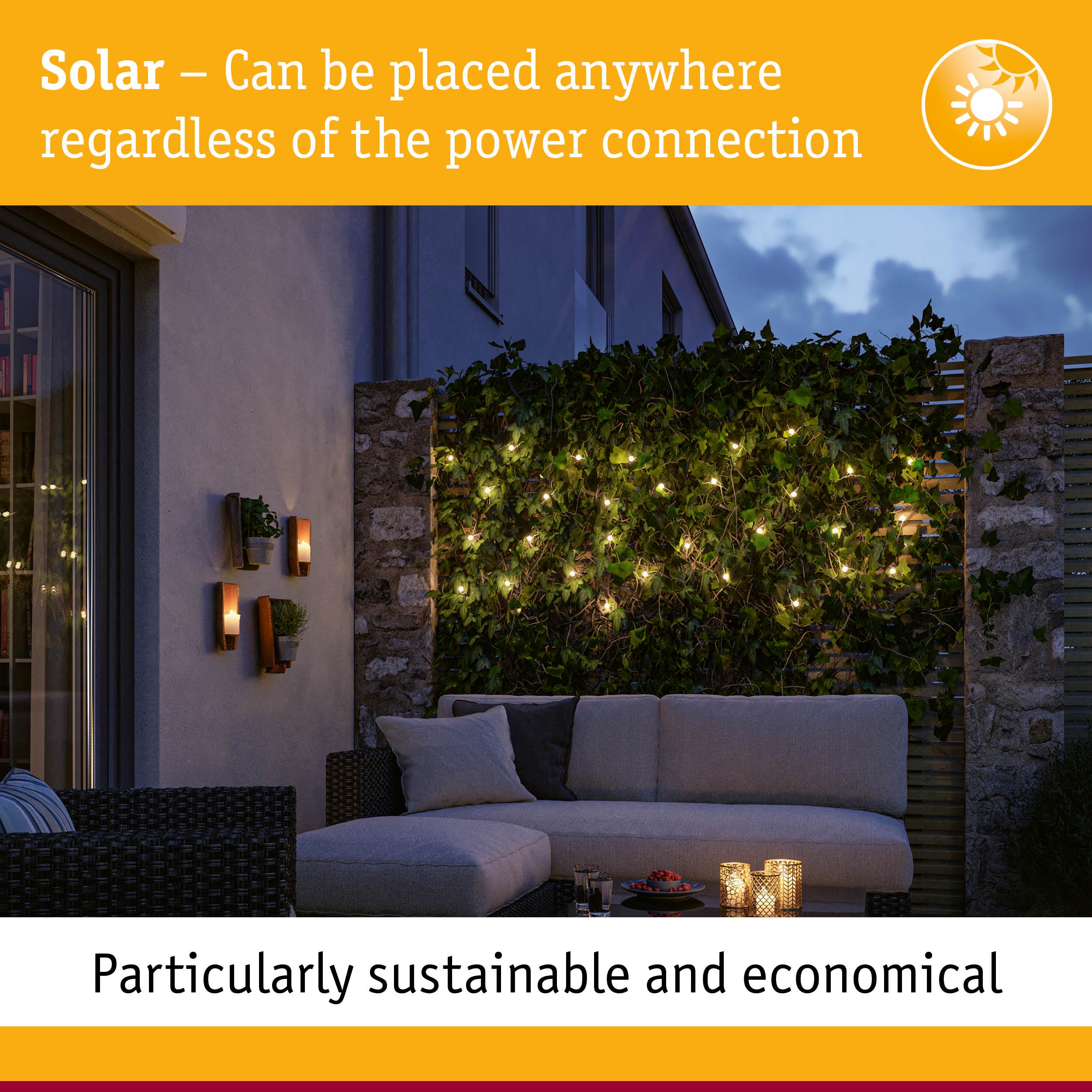 Solar outdoor lights on green hedge with cozy patio sofa at dusk, sustainable garden lighting