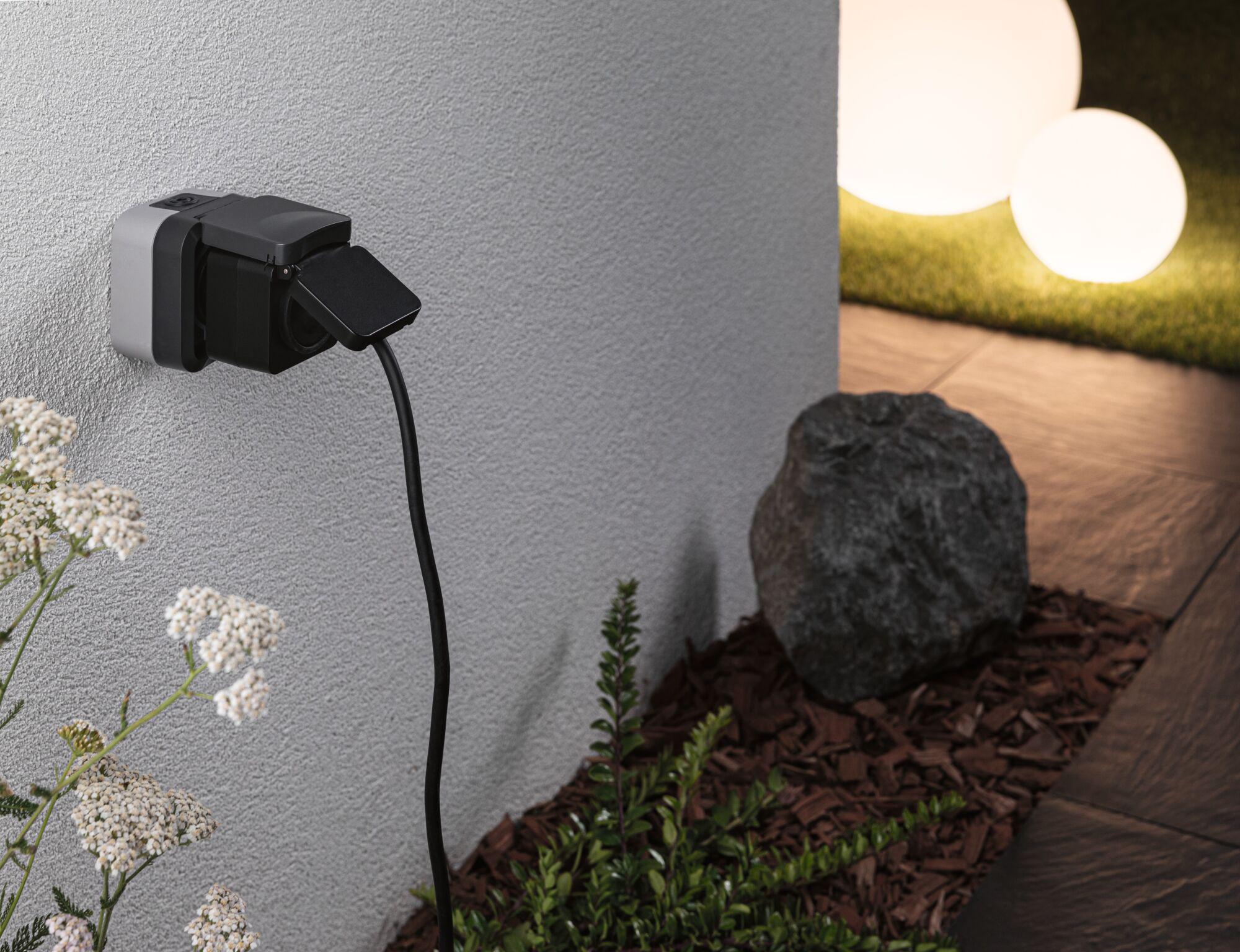 Wasserdichte Außensteckdose in Schwarz und Grau an Hauswand mit Kabel und Gartenbeleuchtung