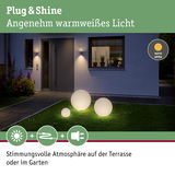Drei weiße Kugelleuchten aus Kunststoff mit warmweißem Licht auf grünem Rasen vor modernem Haus