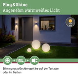Drei weiße Kugelleuchten aus Kunststoff mit warmweißem Licht auf grünem Rasen vor modernem Haus