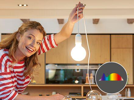 Woman holding glowing LED bulb in modern kitchen, highlighting eye-friendly lighting and color spectrum