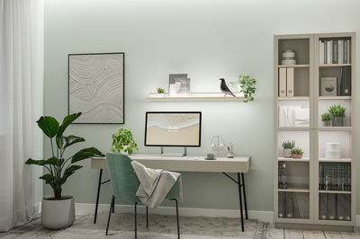 Moderne hjemmekontor med grøn stofstol, lyst skrivebord og LED-væghyldebelysning til arbejdsområde.