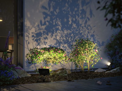 Buiten LED-schijnwerpers met warm wit licht verlichten groene struiken met roze bloemen in tuin 's nachts.