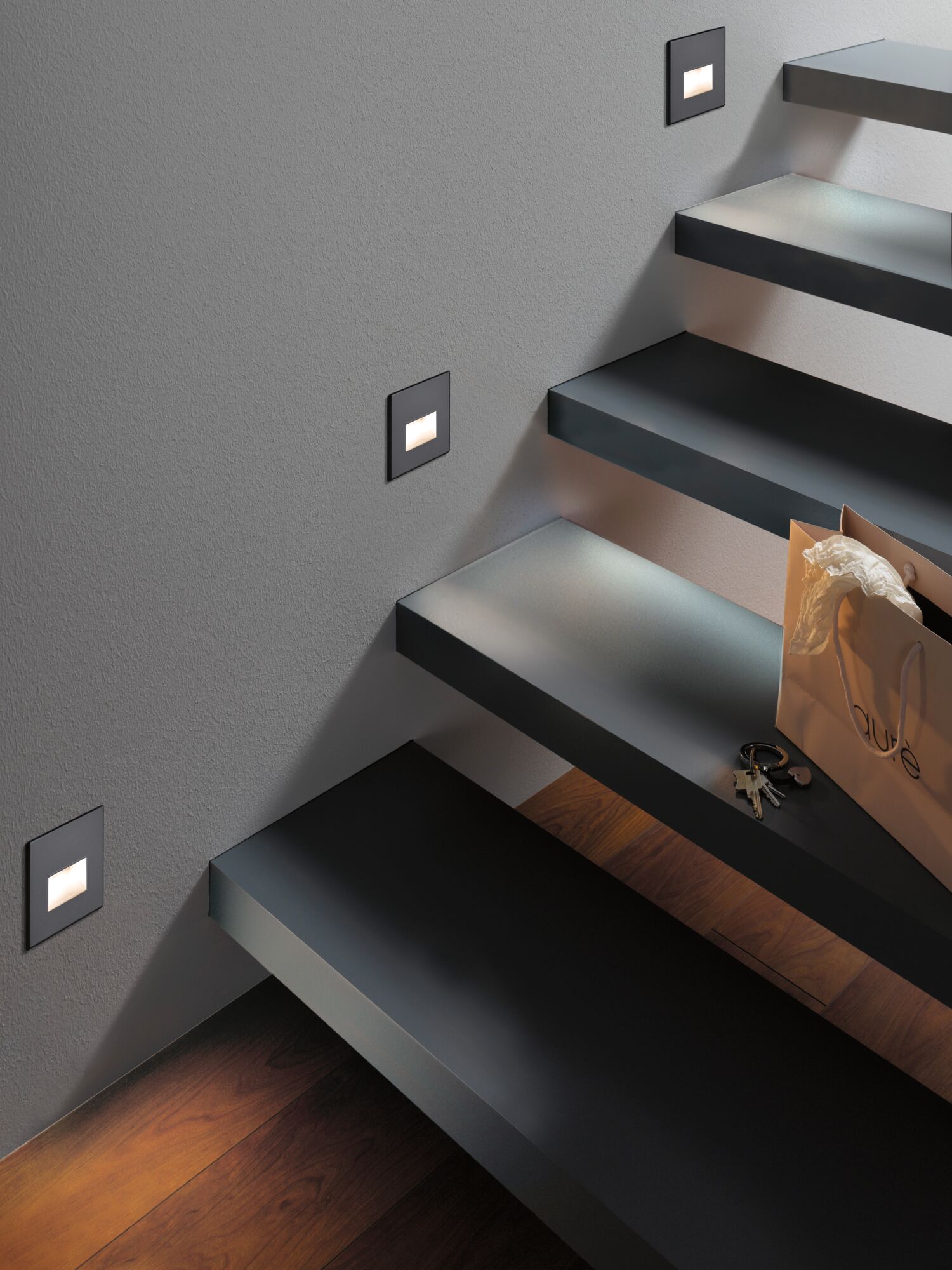 Modern black LED stair lights with warm white illumination on grey wall and wooden floor.