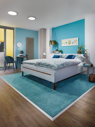 Modernes Schlafzimmer mit weißem Bett, blauem Teppich und LED-Deckenleuchten für gemütliche Beleuchtung