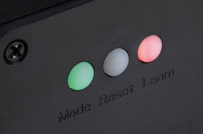 Nahaufnahme von drei LED-Anzeigen in Grün, Weiß und Rot mit Beschriftung Mode Reset Learn auf schwarzem Gerät