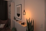 Moderne zwarte metalen hanglamp met warm licht in gezellige woonkamer met planten en wanddecoratie.